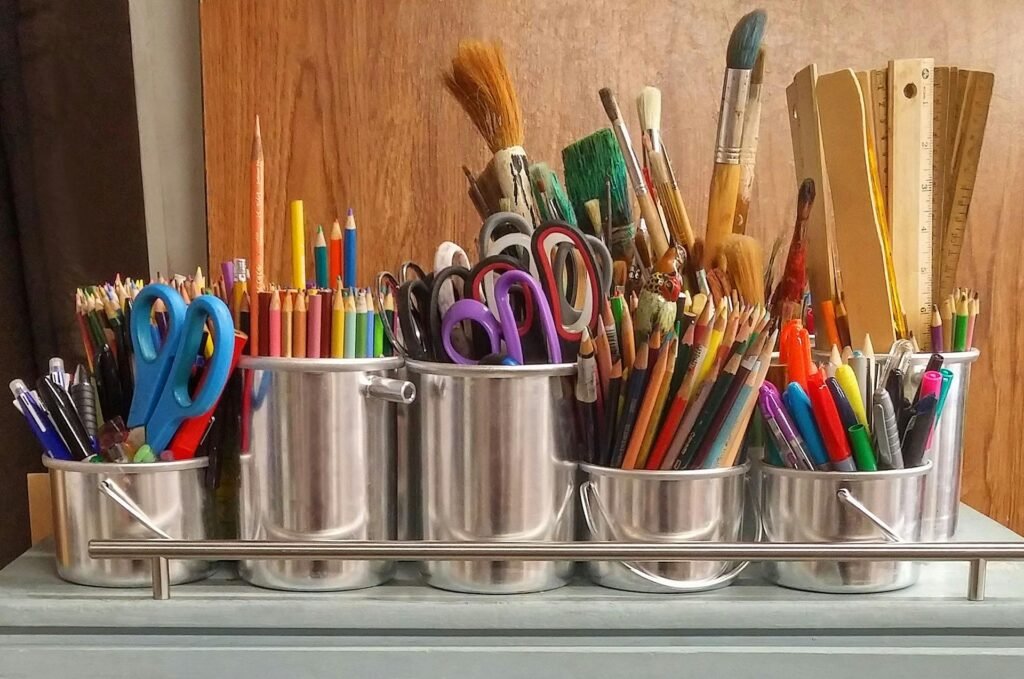 A diverse collection of homeschool arts and crafts supplies in metallic buckets on a wooden table.
