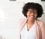 The Farmhouse Smiling businesswoman with glasses and afro hairstyle in an office setting.
